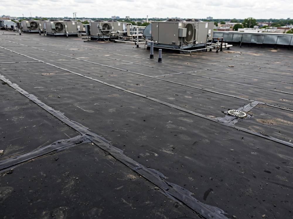 Aerial shot of a large building with a flat concrete rooftop and surrounding grassy area.